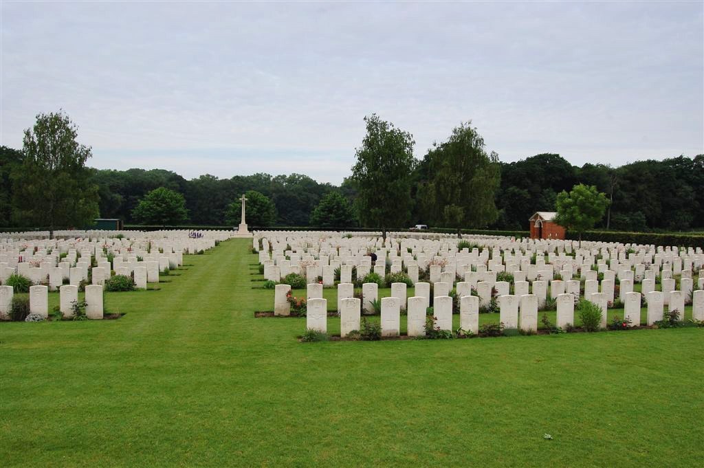 Beautiful sunlit panorama of Dozinghem Military Cemetery, Poperinge, Belgium, showcasing pristine rows of white headstones under a mature tree canopy