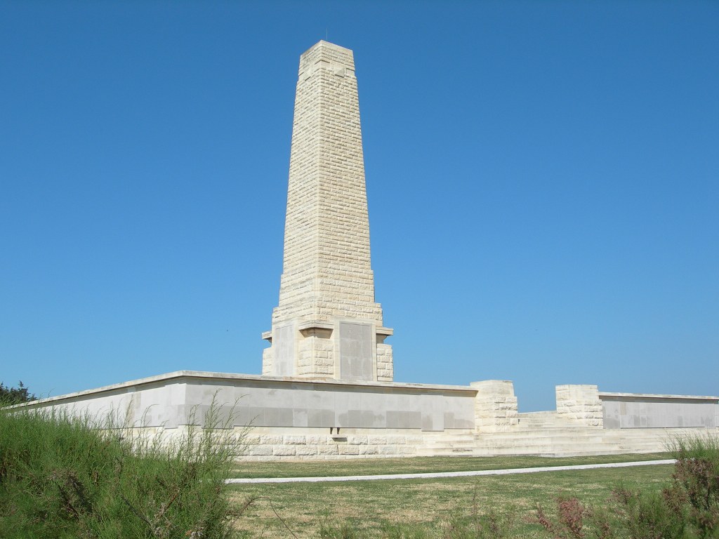 Towering stone obelisk of the Helles Memorial in Gallipoli, Turkey, overlooking the Aegean Sea under a bright blue sky