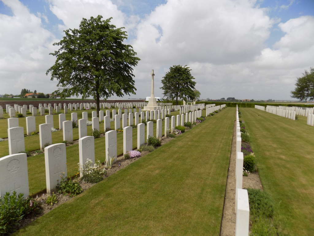 The Huts Cemetery near Ypres, Belgium showing uniform rows of white headstones beneath mature trees